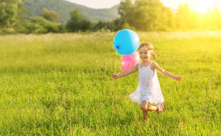 little happy cheerful girl running around playing and having fun with balloons in the summer on the nature